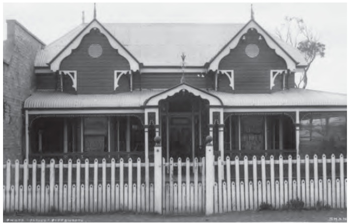 A gable-roofed timber house with a front verandah and ornate white picket fence.